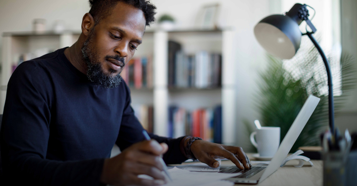 A man sits at a desk making some notes next to his lamp
